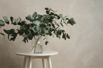 Photo of Beautiful eucalyptus branches in vase on table near light grey wall indoors, space for text