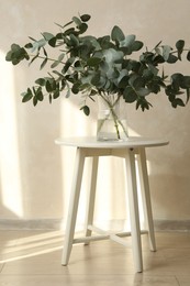 Photo of Beautiful eucalyptus branches in vase on table near light grey wall indoors