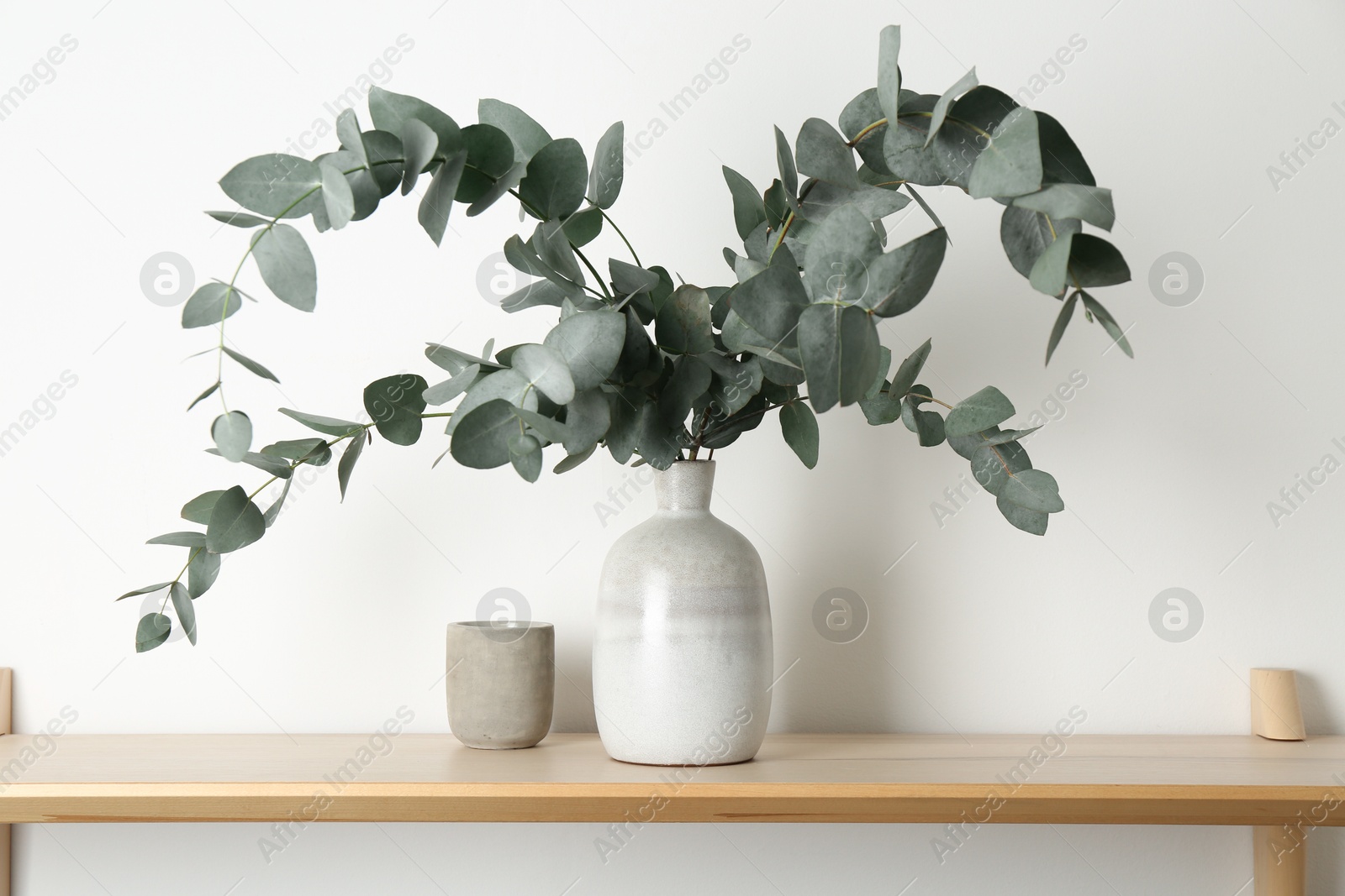 Beautiful eucalyptus branches in vase on wooden table near white wall indoors Photo of Beautiful eucalyptus branches in vase on wooden table near white wall indoors