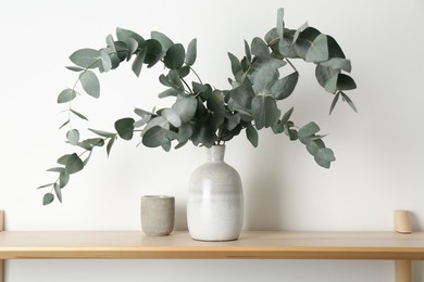Photo of Beautiful eucalyptus branches in vase on wooden table near white wall indoors