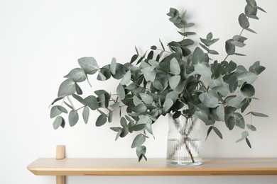 Photo of Beautiful eucalyptus branches in vase on wooden table near white wall indoors