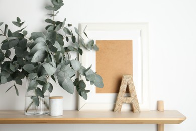 Photo of Beautiful eucalyptus branches in vase and other decor on wooden table near white wall indoors