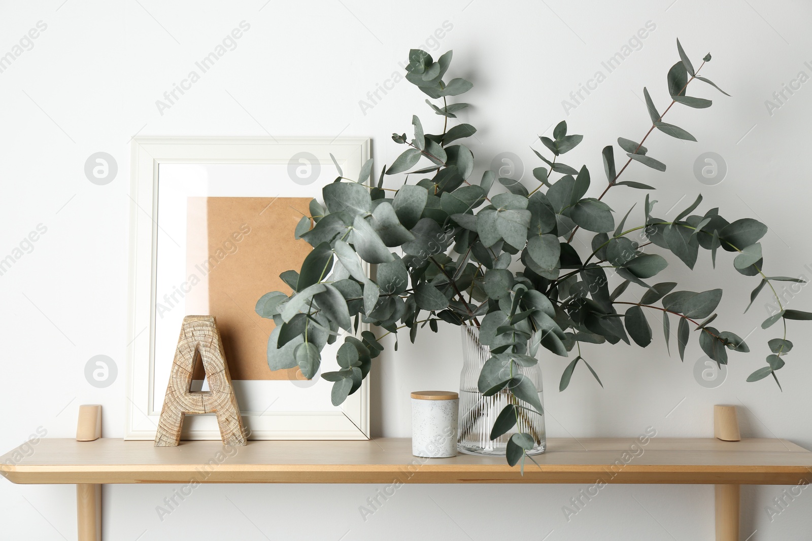 Beautiful eucalyptus branches in vase and other decor on wooden table near white wall indoors Photo of Beautiful eucalyptus branches in vase and other decor on wooden table near white wall indoors