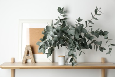 Photo of Beautiful eucalyptus branches in vase and other decor on wooden table near white wall indoors
