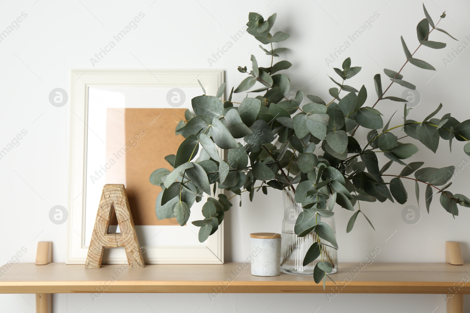 Beautiful eucalyptus branches in vase and other decor on wooden table near white wall indoors Photo of Beautiful eucalyptus branches in vase and other decor on wooden table near white wall indoors