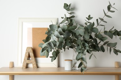 Photo of Beautiful eucalyptus branches in vase and other decor on wooden table near white wall indoors