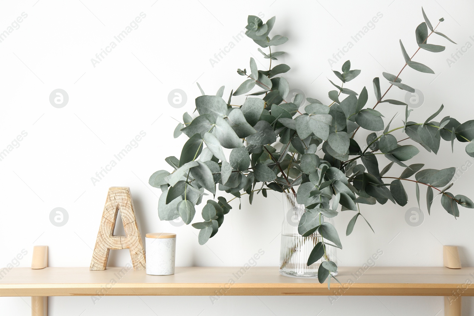 Beautiful eucalyptus branches in vase and other decor on wooden table near white wall indoors Photo of Beautiful eucalyptus branches in vase and other decor on wooden table near white wall indoors