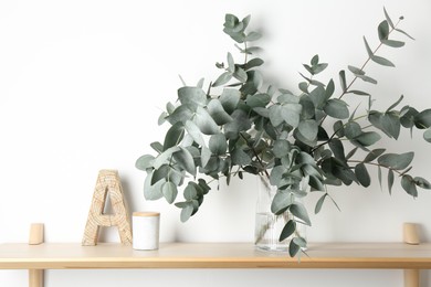 Photo of Beautiful eucalyptus branches in vase and other decor on wooden table near white wall indoors