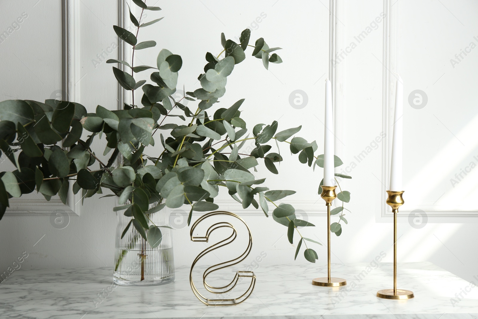Green eucalyptus branches in vase and other decor on marble table near white wall indoors Photo of Green eucalyptus branches in vase and other decor on marble table near white wall indoors