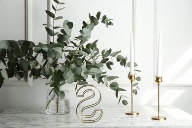 Photo of Green eucalyptus branches in vase and other decor on marble table near white wall indoors