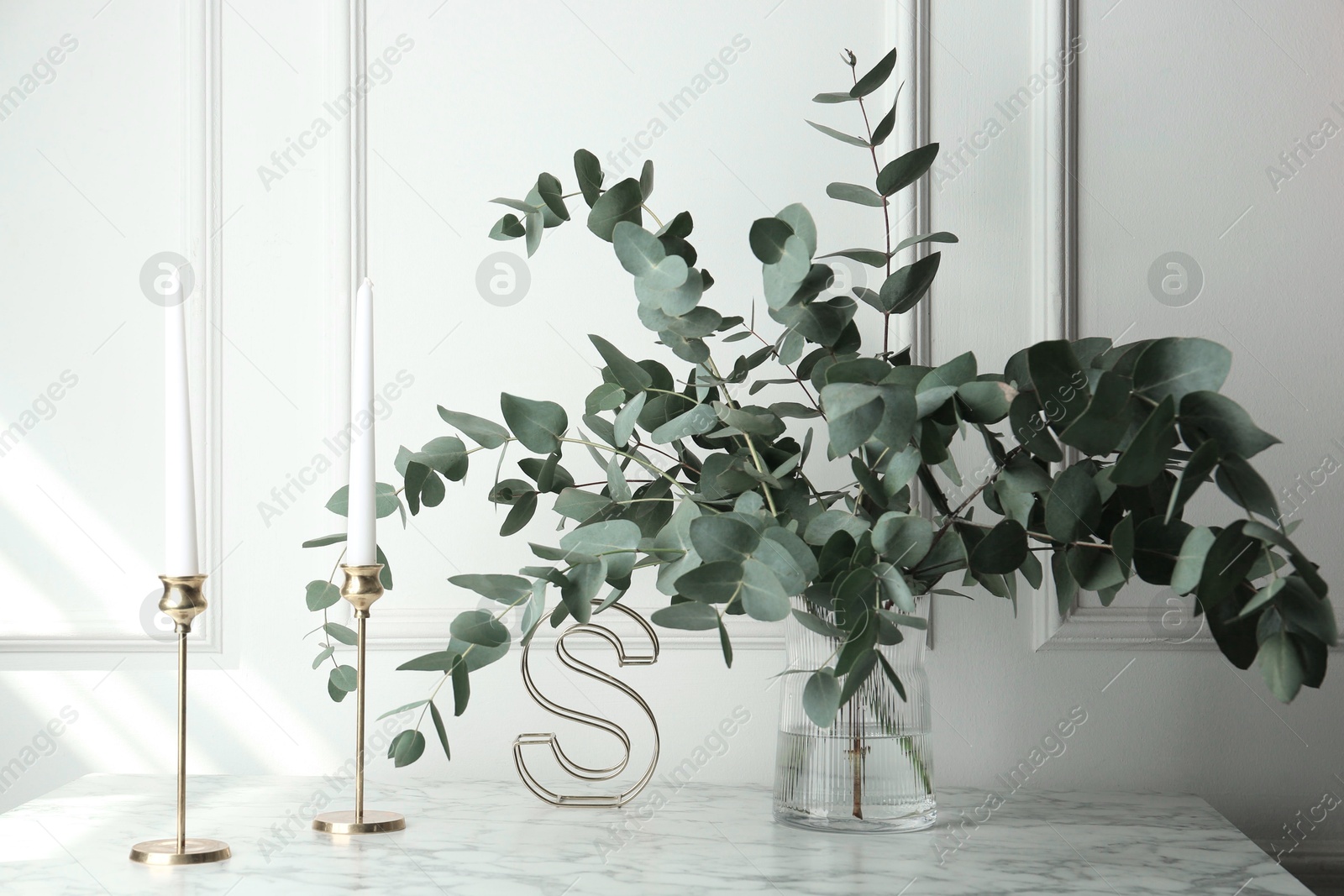 Green eucalyptus branches in vase and other decor on marble table near white wall indoors Photo of Green eucalyptus branches in vase and other decor on marble table near white wall indoors