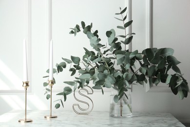 Photo of Green eucalyptus branches in vase and other decor on marble table near white wall indoors