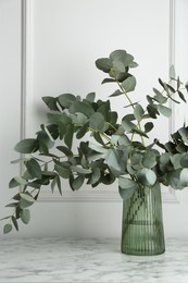 Photo of Green eucalyptus branches in vase on marble table near white wall indoors