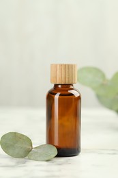 Photo of Bottle of essential oil and eucalyptus leaves on white marble table, closeup