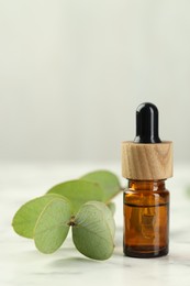 Photo of Bottle of essential oil and eucalyptus leaves on white marble table, closeup