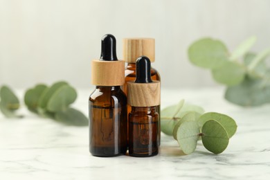 Photo of Bottles of essential oil and eucalyptus leaves on white marble table