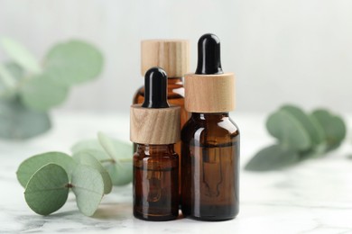 Photo of Bottles of essential oil and eucalyptus leaves on white marble table, closeup