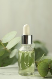 Photo of Bottle of essential oil and eucalyptus leaves on white marble table, closeup