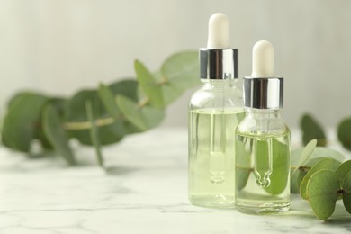 Photo of Bottles of essential oil and eucalyptus leaves on white marble table, closeup. Space for text