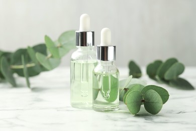 Photo of Bottles of essential oil and eucalyptus leaves on white marble table