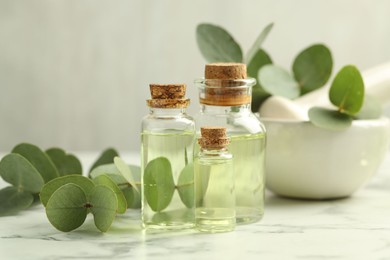 Photo of Bottles of essential oil, eucalyptus leaves, mortar and pestle on white marble table, closeup