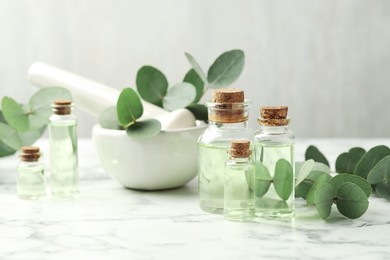 Photo of Bottles of essential oil, eucalyptus leaves, mortar and pestle on white marble table