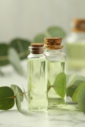 Photo of Bottles of essential oil and eucalyptus leaves on white marble table, closeup