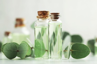 Photo of Bottles of essential oil and eucalyptus leaves on white table, closeup