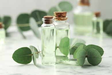 Photo of Bottles of essential oil and eucalyptus leaves on white marble table, closeup
