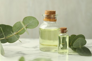 Photo of Bottles of essential oil and eucalyptus leaves on white marble table, closeup