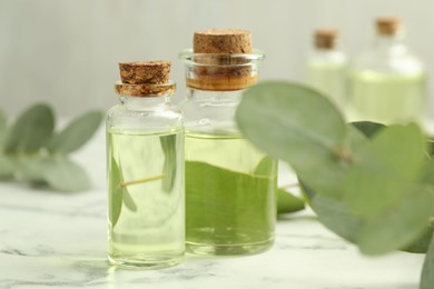Photo of Bottles of essential oil and eucalyptus leaves on white marble table, closeup