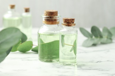 Photo of Bottles of essential oil and eucalyptus leaves on white marble table, closeup