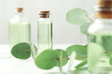 Photo of Bottles of essential oil and eucalyptus leaves on white table, closeup
