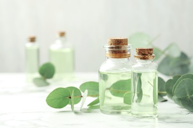 Photo of Bottles of essential oil and eucalyptus leaves on white marble table, closeup