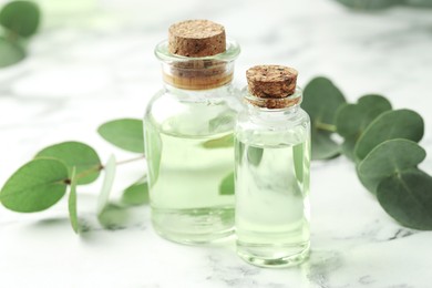 Photo of Bottles of essential oil and eucalyptus leaves on white marble table, closeup