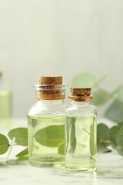 Photo of Bottles of essential oil and eucalyptus leaves on white marble table, closeup