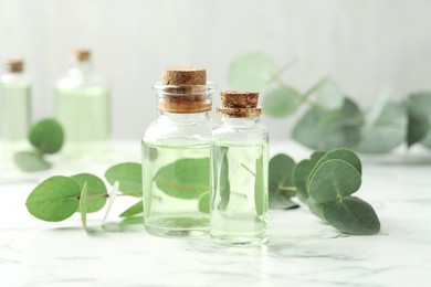 Photo of Bottles of essential oil and eucalyptus leaves on white marble table