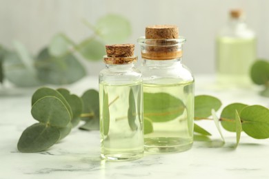 Photo of Bottles of essential oil and eucalyptus leaves on white marble table, closeup