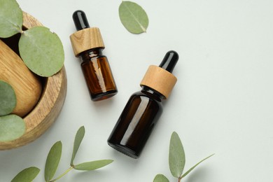 Photo of Bottles of essential oil, eucalyptus leaves, mortar and pestle on white background, flat lay