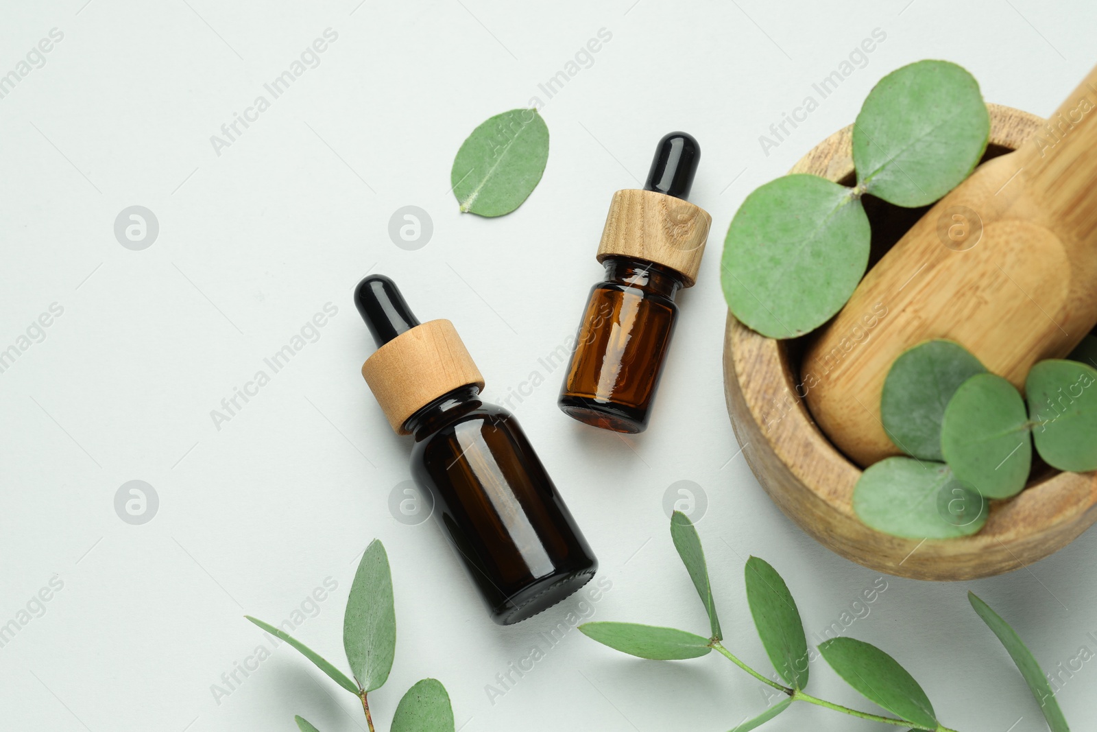 Bottles of essential oil, eucalyptus leaves, mortar and pestle on white background, flat lay Photo of Bottles of essential oil, eucalyptus leaves, mortar and pestle on white background, flat lay