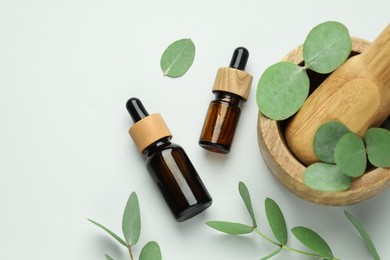 Photo of Bottles of essential oil, eucalyptus leaves, mortar and pestle on white background, flat lay