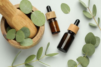 Photo of Bottles of essential oil, eucalyptus leaves, mortar and pestle on white background, flat lay