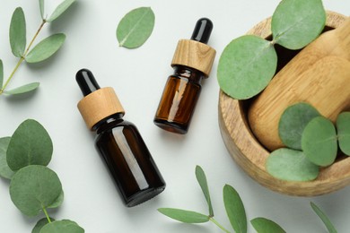 Photo of Bottles of essential oil, eucalyptus leaves, mortar and pestle on white background, flat lay