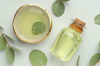 Photo of Bottle of essential oil, bowl and eucalyptus leaves on white background, flat lay