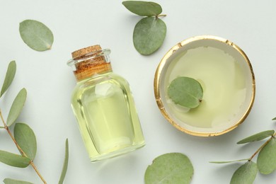 Photo of Bottle of essential oil, bowl and eucalyptus leaves on white background, flat lay