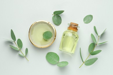 Photo of Bottle of essential oil, bowl and eucalyptus leaves on white background, flat lay