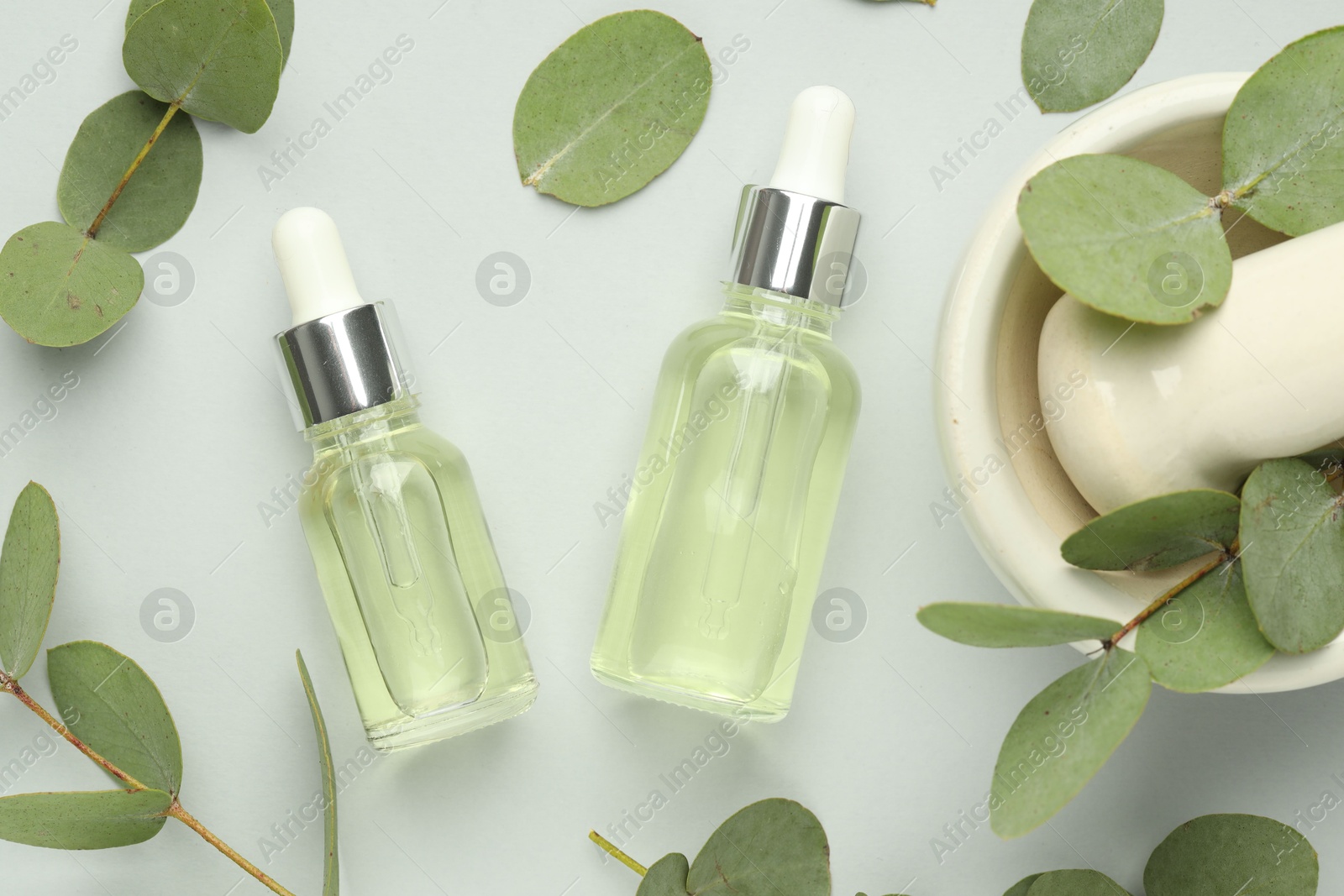 Bottles of essential oil, eucalyptus leaves, mortar and pestle on white background, flat lay Photo of Bottles of essential oil, eucalyptus leaves, mortar and pestle on white background, flat lay