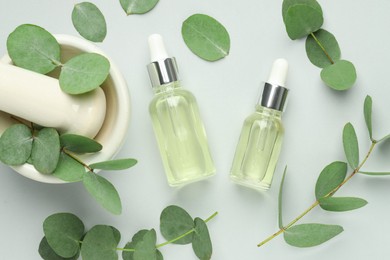 Photo of Bottles of essential oil, eucalyptus leaves, mortar and pestle on white background, flat lay