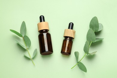 Photo of Bottles of essential oil and eucalyptus leaves on green background, flat lay