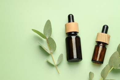 Photo of Bottles of essential oil and eucalyptus leaves on green background, flat lay. Space for text